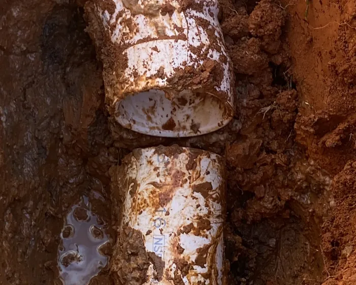 A section of white sewer pipe exposed in an open hole in Gaston County red clay during a line repair